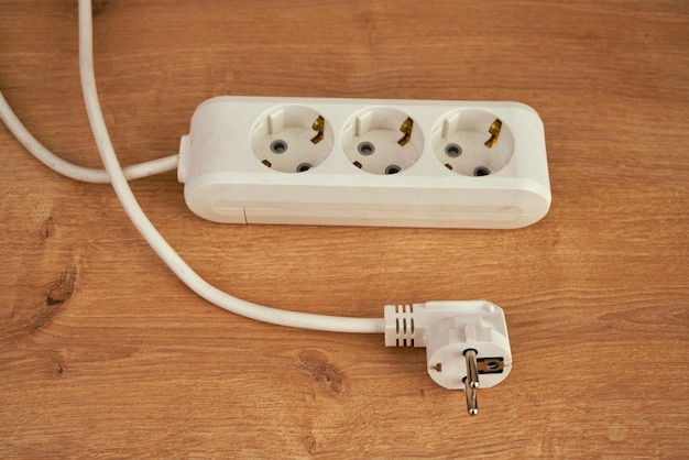 White triple extension socket with long cable on a wooden surface.