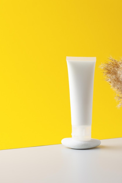 White tube of cosmetic cream on a stone podium with pampas on yellow background close up