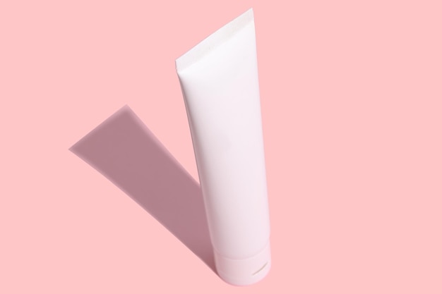 White tube of cosmetic cream with a hard black shadow on a pink background