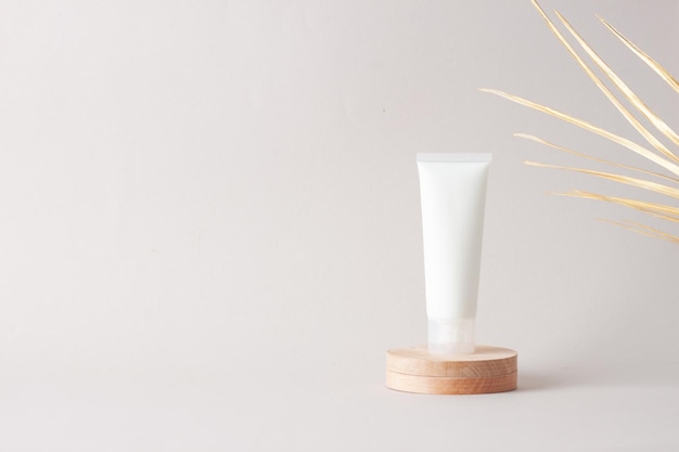 White tube of cosmetic cream with wood podium and palm leaf on grey background Close up copy space