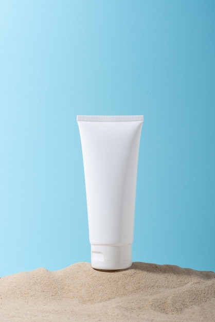 White tube of cream moisturizer on sand on blue background
