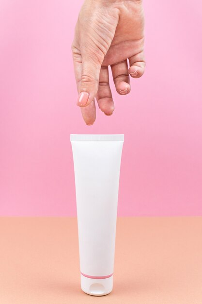 White tube with cream in a womans hand Closeup of cosmetic product on pink and orange background