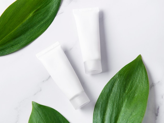 White tubes of cream on a marble background with green  leaves