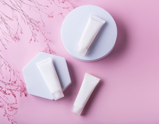 White tubes of cream on a pink background and decorative branch