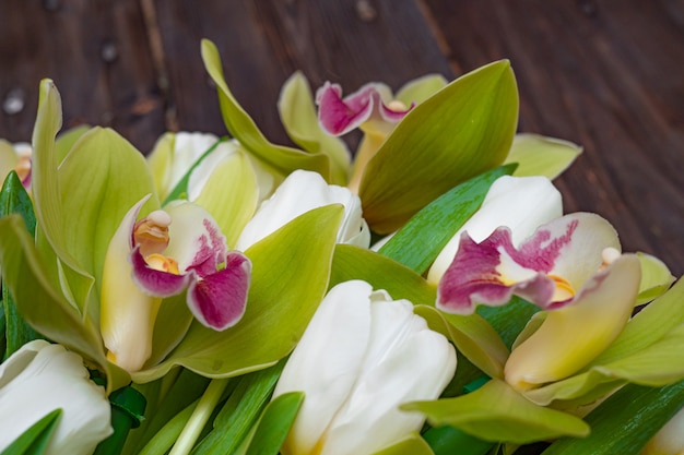 White tulips and green orchids on a dark wooden table