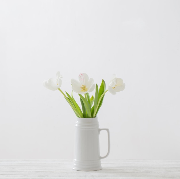 White tulips in jug on white background