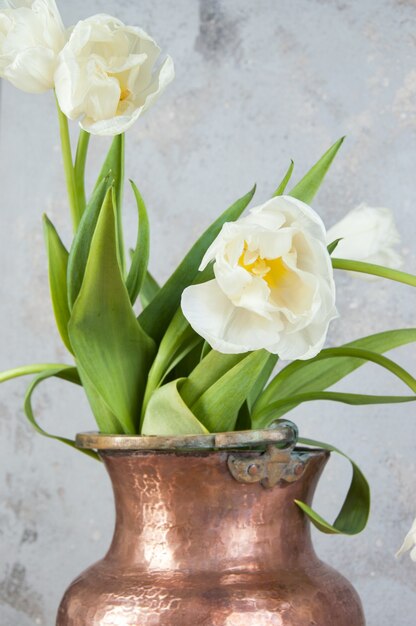 古い銅の花瓶の白いチューリップ