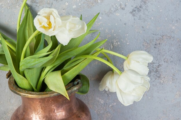 Tulipani bianchi in un vecchio vaso di rame