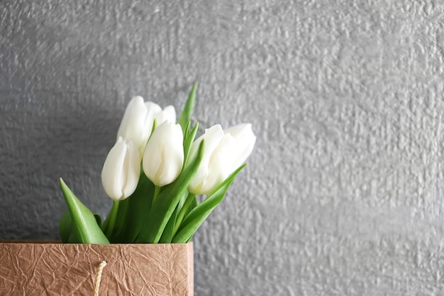 Tulipani bianchi in sacchetto di carta sul tavolo di legno contro il muro grigio da vicino