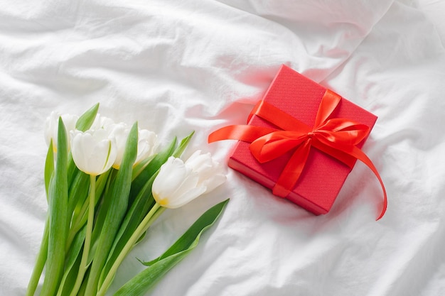 White tulips red gift box on bed Still life Minimal concept Womans day Mothers day holiday