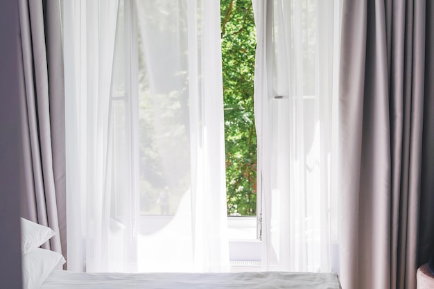 White tulle curtains on the window with green trees on background at home