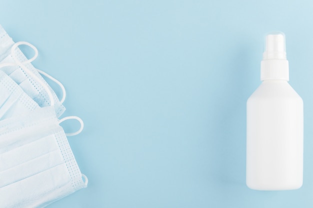 White unbranded bottle of sanitizer and medical protective mask on table. COVID-19 and quarantine.