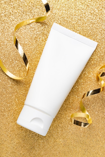 White unbranded tube with hand cream or face mask on glittering golden background Beauty treatment presentation for holidays as a gift