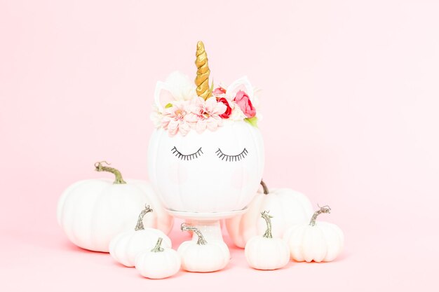 White unicorn pumpkin decorated with flowers on a pink background.