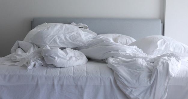 White unmade bed with crumpled messy blanket and pillow in morning light