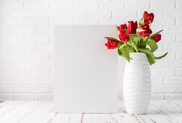 White vase with red tulips next to a ampty board for your text White background