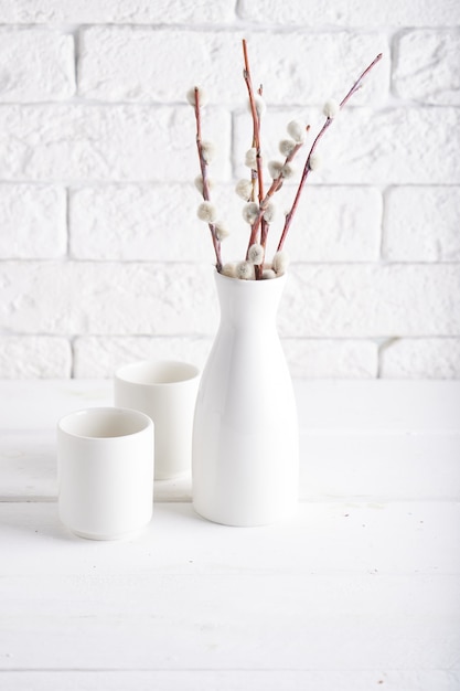 White vase with willow branch and cups on a white table Copy space Vertical