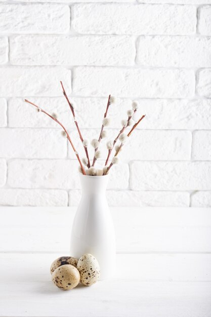 White vase with willow branch , quail eggs and cups on a white table Copy space Easter concept