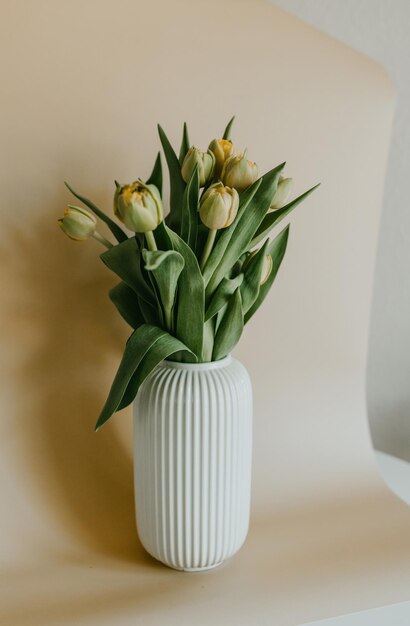 A white vase with yellow tulips on a table