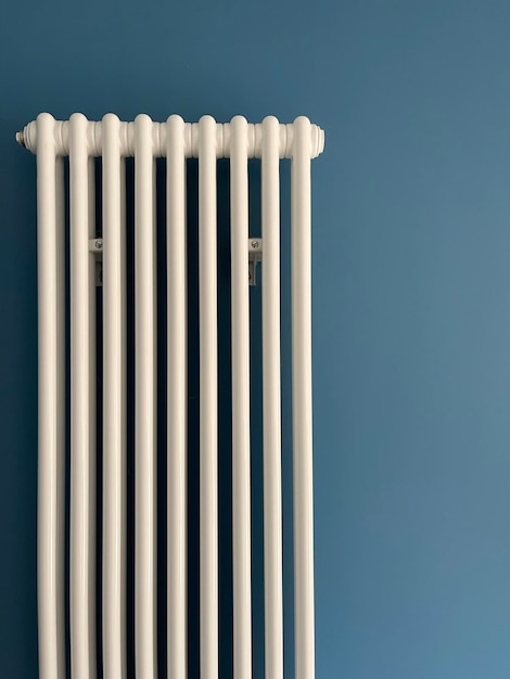 White vertical heating system radiator on blue wall