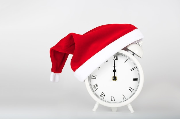 White vintage alarm clock on a gray background in a Santa Claus hat.