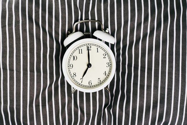 White vintage alarm clock on pillow in bed.