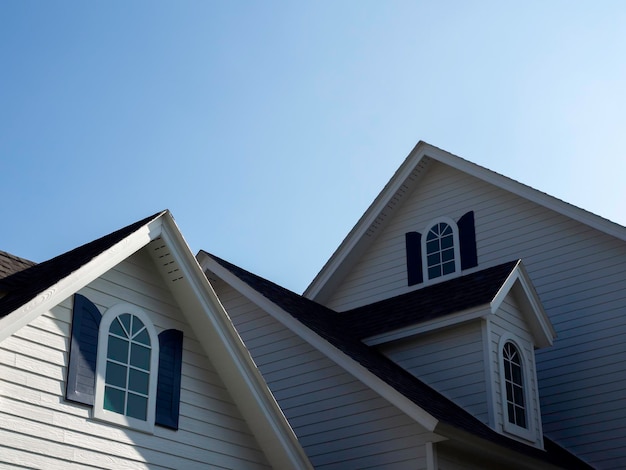 Photo white vintage curved frame windows, little room decoration on the roof of the big white wooden house on blue sky background with copy space, view from outside.