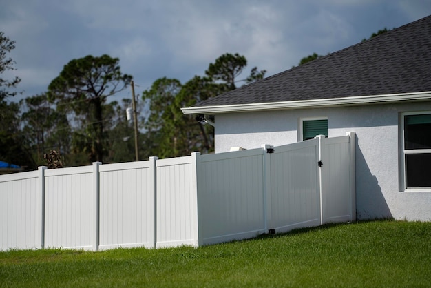 White vinyl picket fence on green lawn surrounding property grounds for backyard protection and privacy