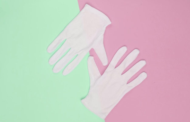 Белые перчатки официанта на розовом зеленом пастельном фоне. Вид сверху