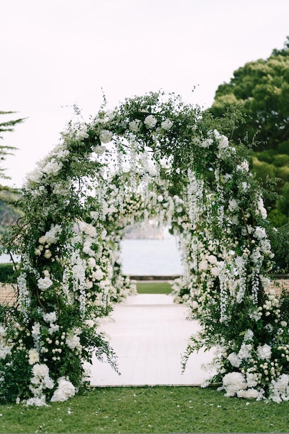 緑の芝生の上の結婚式のアーチの列を通る白い通路