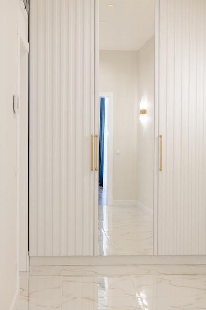 A white wardrobe with a mirror in the hallway
