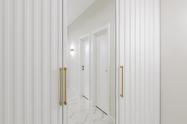 A white wardrobe with a mirror in the hallway