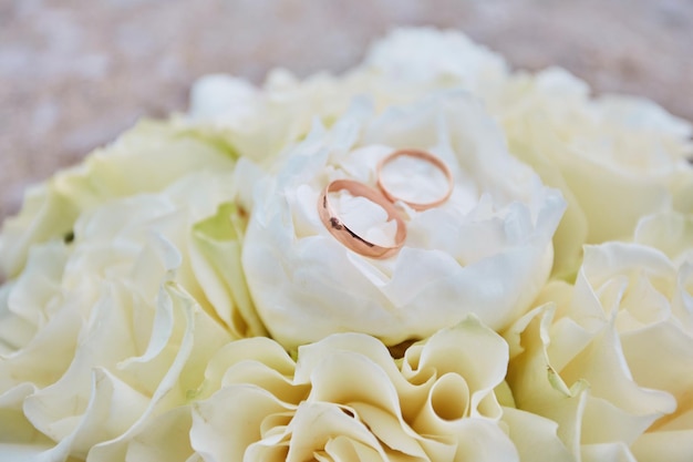 バラの白いウェディングブーケとその上の結婚指輪のペア