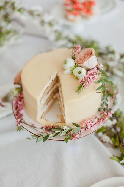 White wedding cake on white tablecloth decorated with flowers and greenery boho style wedding