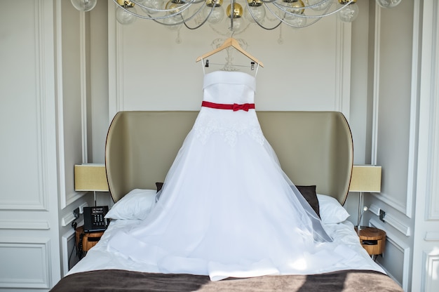 White wedding dress of the bride hanging on the chandelier in the hotel room