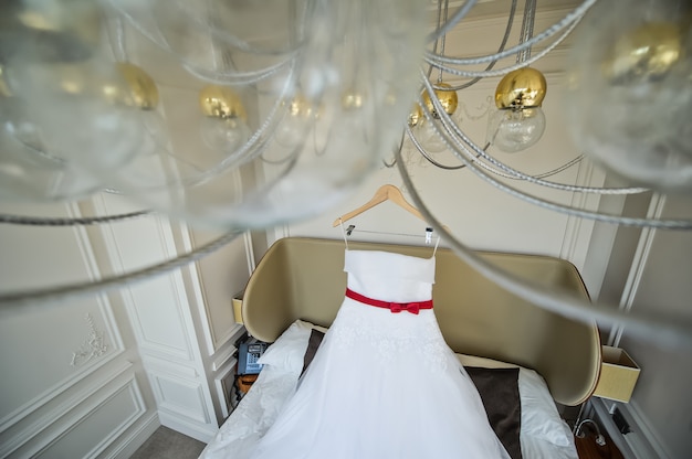 White wedding dress of the bride hanging on the chandelier in the hotel room