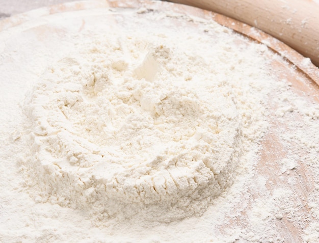 White wheat flour heaped on a round wooden board top view