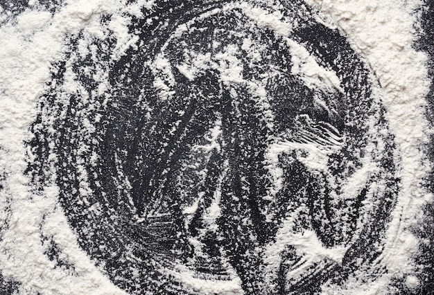 White wheat flour scattered on a black wooden table, top view