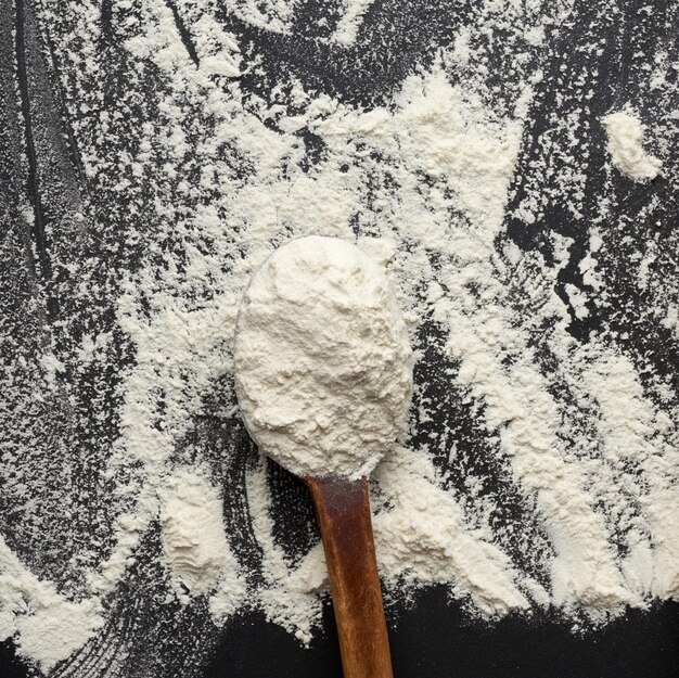 White wheat flour in a wooden brown spoon, black space