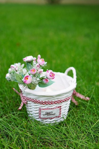 White wicker basket with decorative pink roses stands on green grass in the middle of the garden