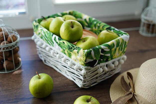 A white wicker basket with green apples on a wooden table near the window