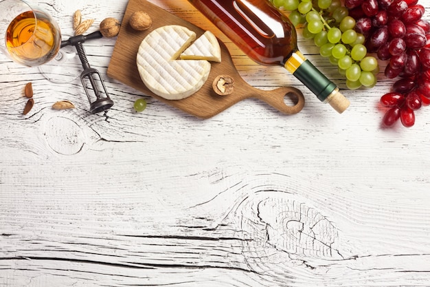 White wine bottle, grape, cheese and wineglass on white wooden board