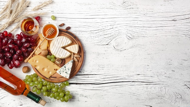 White wine bottle, grape, honey, cheese and wineglass on white wooden board