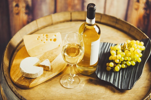 White wine in glass bottle with grape and cheese on barrel front wood wall background