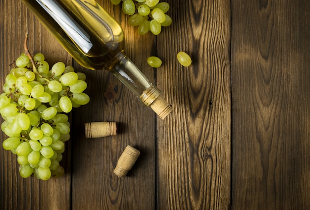 White wine with branches of white grapes. On a wooden table.