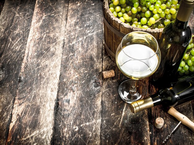 White wine with a bucket of green grapes. On a wooden table.