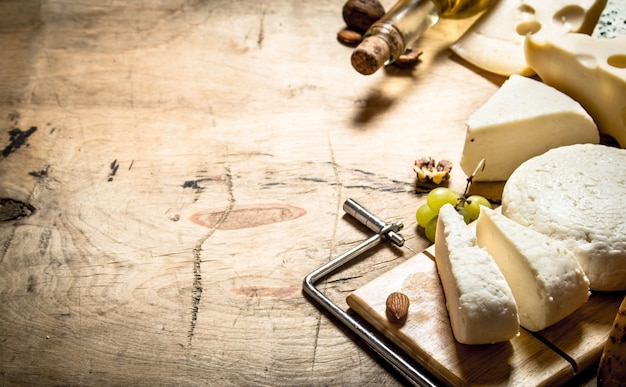 White wine with different types of cheese on wooden table.