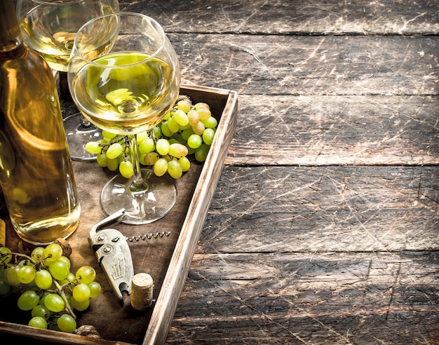 White wine with fresh grapes on an old tray. On a wooden table.