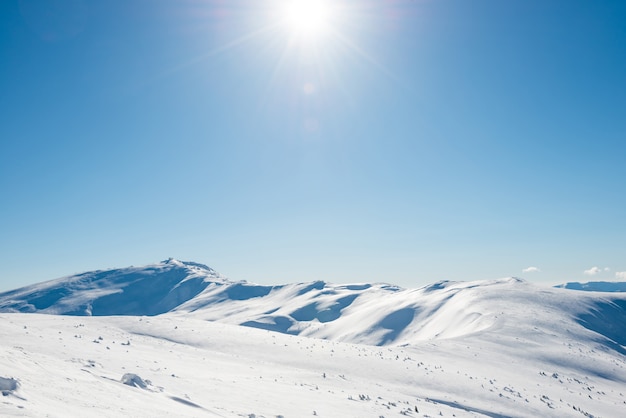 雪と明るく輝く太陽と太陽光線のある白い冬の山々