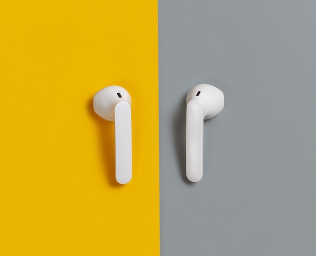 White wireless earphones on yellow and grey background  top view